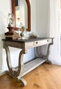 an old table with books on it and a mirror in the corner behind it,