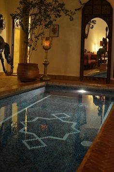 an indoor swimming pool with decorative tile in the middle and potted plant next to it