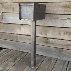 a metal mailbox sitting on top of a wooden deck next to a wall covered in wood planks