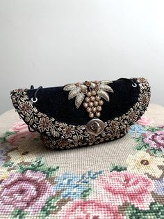 A fantastic little vintage handbag in black velvet with gold and bronze coloured wire work embroidery and faux pearls. The bag is an unusual shape, almost boat shaped and has a simple cord handle which is knotted at the top. It fastens with a metal swivel lock. Inside is lined in black silky fabric with one internal pocket. It feels like the inner carcass of the bag is made with firm card, so it will hold its shape like a small box.  The base of the bag measures approx 2.5 x 5 inches with an int Antique Gold Embroidered Bags, Victorian Style Gold Embroidered Bag, Vintage Gold Embroidered Clutch, Gold Vintage Clutch With Embroidery, Gold Shoulder Bag With Zari Work For Evening, Evening Gold Shoulder Bag With Zari Work, Vintage Gold Bag With Handwork, Vintage Gold Bags With Handwork, Vintage Embroidered Evening Bag For Festive Occasions