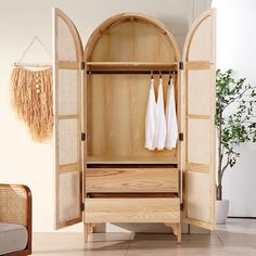 an open wooden cabinet with two white towels hanging on it's doors and some plants in the background