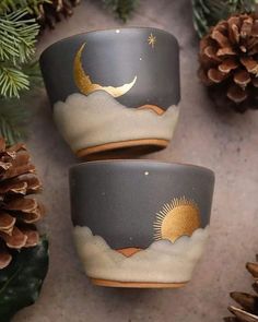 two cups sitting on top of a table next to pine cones and evergreen branches with the moon in the sky