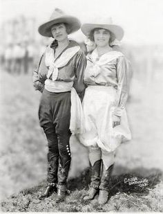 an old photo of two women standing next to each other wearing hats and dress clothes