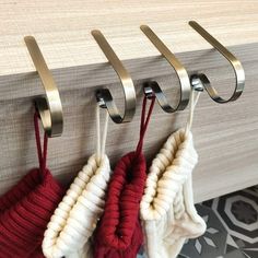 three knitted mitts hanging from hooks on a wall