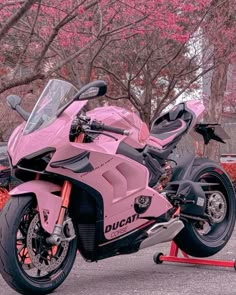 a pink motorcycle parked on top of a red stand in front of some trees and bushes