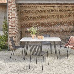 an outdoor table with four chairs in front of a brick wall and potted plants