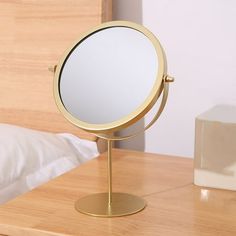 a mirror sitting on top of a wooden table next to a night stand with a bed in the background