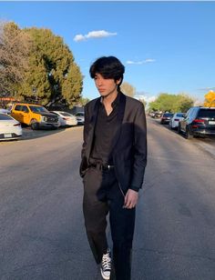 a man walking down the middle of a street wearing a black suit and white sneakers