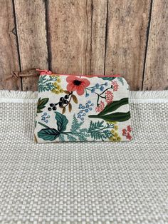 a small purse with flowers and leaves on it sitting next to a wooden wall or floor