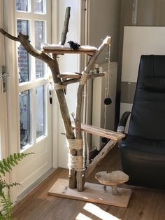 a tree made out of branches in front of a window with a black chair next to it