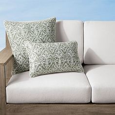 two pillows sitting on top of a white couch next to a wooden rail and blue sky