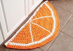 a crocheted orange rug on the floor in front of a white cabinet door