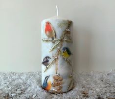 a candle with birds painted on it sitting on top of a pile of white snow