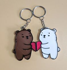 two bears holding a heart shaped object on a keychain that is attached to each other