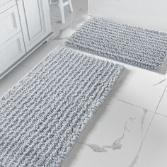 two gray rugs sitting on top of a white floor next to a kitchen counter