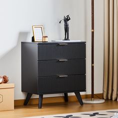 a black cabinet with three drawers and a small statue on top, in front of a window