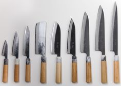 several knives are lined up in a row on a white surface with wooden handles and blades