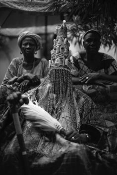 two men sitting next to each other in front of a tree with an elaborate headdress