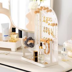 a white desk topped with lots of gold jewelry and perfume bottles next to a mirror