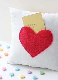 a pillow with a red heart on it and a note attached to the back that says i love you