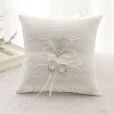 a white pillow with two wedding rings tied to the side on a lace covered bed