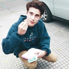 a young man sitting on the ground holding a book