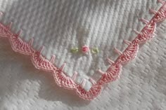 an embroidered piece of cloth on top of a white tablecloth with pink trimmings