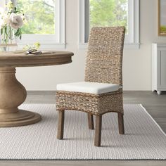 a wicker dining room chair next to a round table with flowers on the side