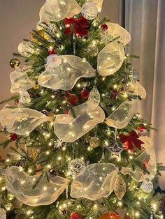 a white christmas tree with red and gold ornaments on it's branches, surrounded by lights