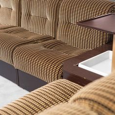 a brown and white checkered couch sitting next to a wooden table on top of a carpeted floor