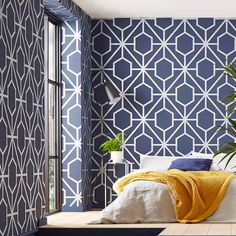 a bedroom with blue and white wallpaper that has geometric designs on it, along with a plant next to the bed