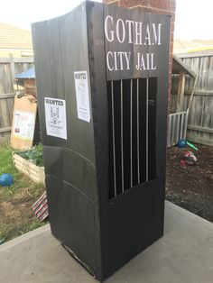 a black trash can sitting on the side of a sidewalk next to a fence and yard