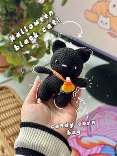 a hand holding a black crocheted teddy bear with candy corn in it's mouth