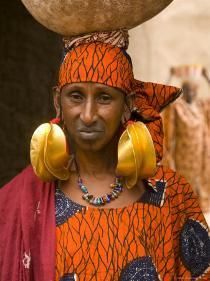 an african woman carrying a large pot on her head and wearing earring's