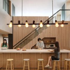 two people sitting at a counter in a kitchen with lights hanging from the ceiling above them