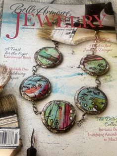 the front cover of a magazine with four pendants and paintbrush next to it