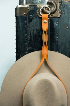 a hat hanging from a hook on the back of a suit case with an orange ribbon around it