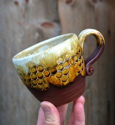 a hand holding a ceramic cup with honeycombs on it's rim and handle