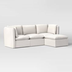 a white sectional couch with pillows on the top and bottom, sitting in front of a gray background