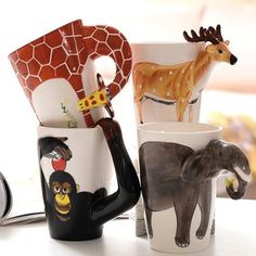 four coffee mugs with animal designs on them sitting on a table next to a clock