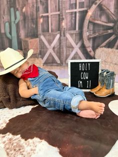 a baby doll laying on top of a cow skin rug next to a cowboy hat