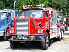 a red fire truck parked next to other trucks in a parking lot with trees in the background