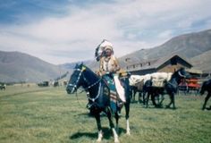 a native american man riding on the back of a black horse with other horses in the background