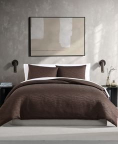 a bed with brown comforter and pillows in a white room next to a painting on the wall