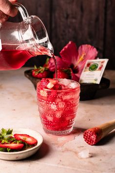 someone is pouring water into a glass with strawberries in it