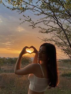 a beautiful young woman standing in front of a tree making a heart shape with her hands