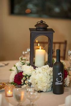 a candle and some flowers on a table with wine bottles, glasses and silverware