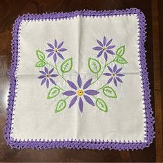 a purple and green floral design on a white cloth with crocheted edges,