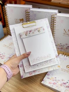 a hand holding a clipboard next to three notebooks on a table with flowers