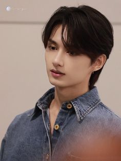 the young man is wearing a denim shirt and looking off to the side with his hand on his hip